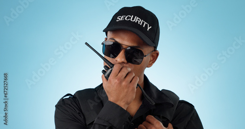 Security, radio and an officer man on a blue background in studio for surveillance or communication. Face, uniform and sunglasses with a young law person speaking on a walkie talkie for patrol