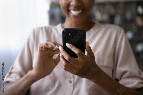 Happy African American young woman using app on mobile phone, reading funny text message, laughing, enjoying online chat, dating flirt, getting good news from nice video call talk. Close up of hands