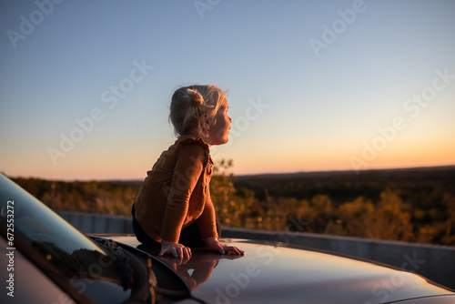 Child sitting on car at overlook watching autumn sunset © Cavan