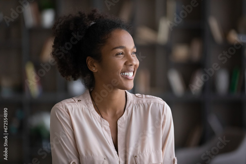 Happy African American millennial girl, young woman feeling joy, having fun, positive mood, looking away, thinking over successful future opportunities, smiling at good thoughts. Head shot portrait