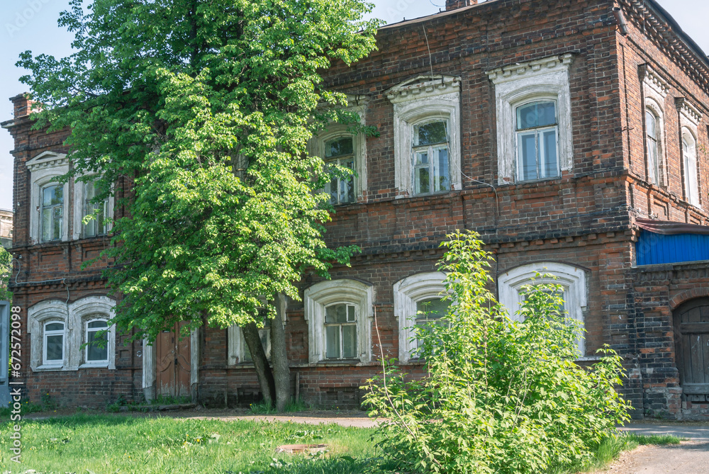 Fototapeta premium An old brick building built in the 19th century. The facade of an old house. An old house in need of repair. An old brick house and trees. Architecture of the last century.