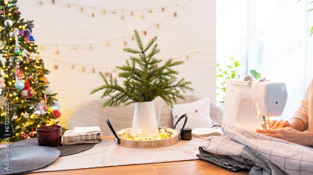 Sewing process on a sewing machine, women hands control needle with a thread white checkered fabric. Preparation for Christmas and new year, textiles for cozy in festive decor interior