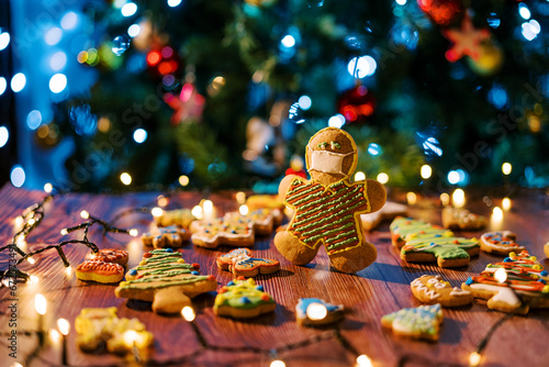 Cookie-man in a mask stands on the table among spread glazed cookies and shining garlands