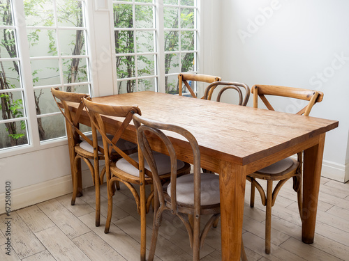 Empty vintage wood dining table set with 6 old chairs seat on wood pattern rubber tiles near glass window with tree outside and white background. Bright clean dining room with nobody, rustic style.