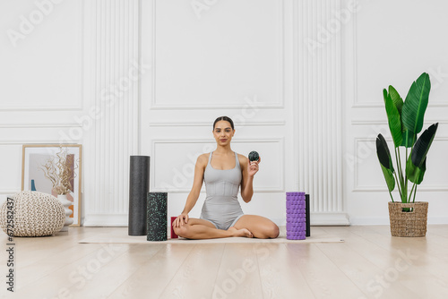 A young athletic woman trainer is ready for training, surrounded by sports equipment for a healthy and beautiful female body. Relieves back tension and relieves muscle pain.