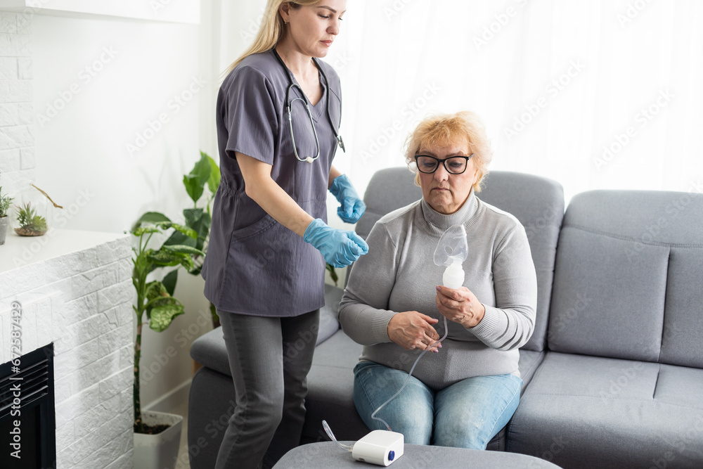 Obraz premium Young high-skilled pleasant woman doctor putting on nebulizer mask on face of her elderly female patient to make inhalation when visitng him at home. Flu, cold and cough treatment