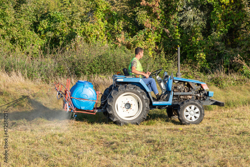 Male gardener on a Mini-tractor. Maintenance of the territory, sprays territory with insecticide for mosquitoes or pests or herbicides for weeds. photo