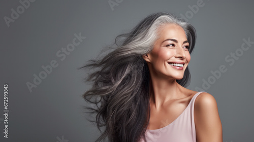 Sensual middle-aged beautiful Asian woman with long grey hair, her eyes closed, body and face care concept. Charming mature lady stands in profile isolated on grey studio background photo