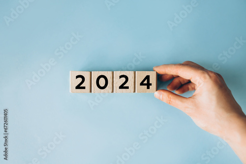 Female hand putting wooden cube for countdown to 2024. Loading year from 2023 to 2024. New year start concept