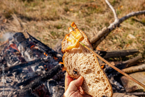 a man hand holds a slice of toasted bread with fried bacon an open fire in nature, slanina,traditional food in Romania photo