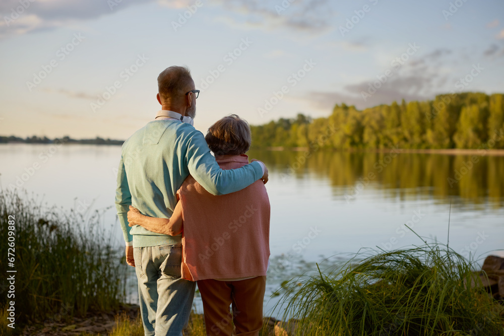 Romantic calm senior couple looking faraway standing at river bank