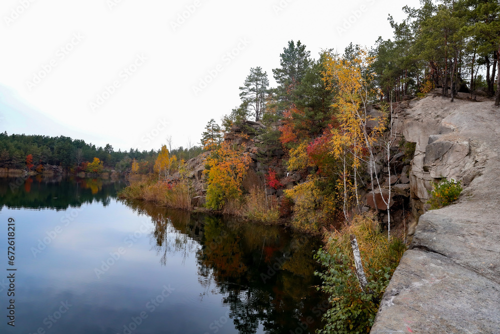 granite rocks on the shore of a flooded quarry, colorful autumn trees growing on the rocks granite rocks on the shore of a flooded quarry, colorful autumn trees growing on the rocks