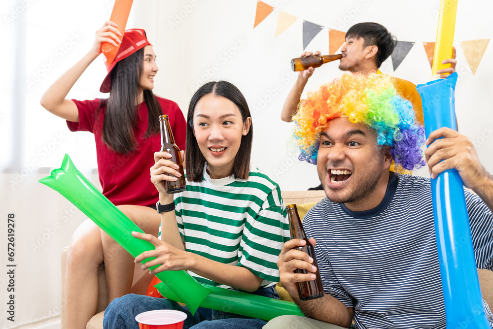 Fototapeta premium Happy asian diverse group friends watching soccer games world cup competition on television together at home with snack and beer. Sport fans people shouting and celebrating sport team victory match.