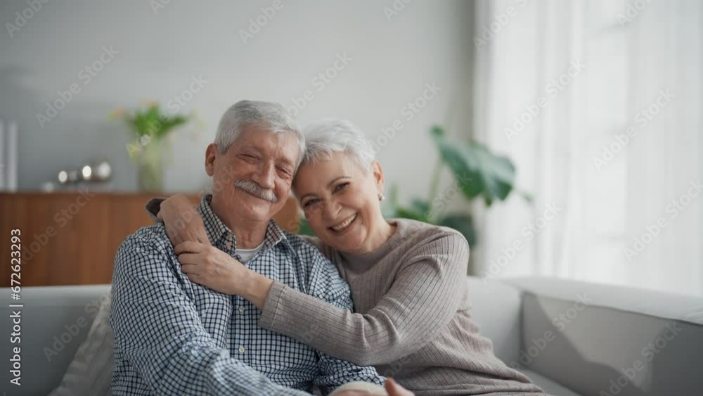 Portrait of senior couple laughing hugging sitting on couch in living room at home, elderly wife and husband in lifelong relationships, happy marriage concept. Old gray haired people look at camera. Portrait of senior couple laughing hugging sitting on couch in living room at home, elderly wife and husband in lifelong relationships, happy marriage concept. Old gray haired people look at camera.