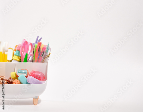 Different colored pens, paint brushes, paper clips, markers and scissors in a white bathtub shaped stationery stand isolated. Copy space for text.