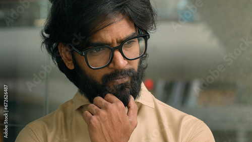 Thoughtful worried Arabian businessman thinking of future business challenges financial crisis. Doubtful serious pensive Indian bearded man in glasses entrepreneur lost in thoughts think about problem