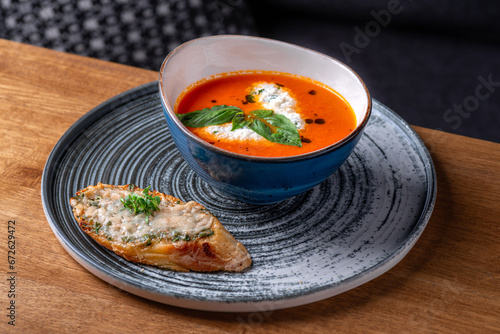 Bowl of tomato soup drizzled with cream and garnish with leaves of fresh green basil