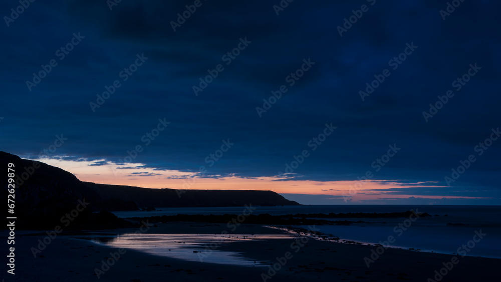 Fototapeta premium Beautiful sunrise landscape image of Kennack Sands in Cornwall UK wuth dramatic moody clouds and vibrant sunburst