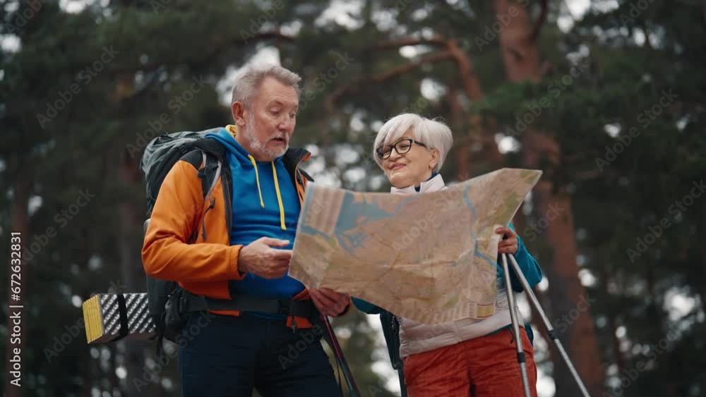 Senior couple hikers man woman hiking on nature talking discussing finding route look at paper map. Tourists trekking carrying backpacks with touristic equipment. Travel tourism wanderlust concept. Senior couple hikers man woman hiking on nature talking discussing finding route look at paper map. Tourists trekking carrying backpacks with touristic equipment. Travel tourism wanderlust concept.