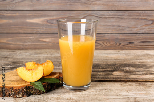 Glass of delicious peach juice, cut fresh fruit and leaves on wooden table