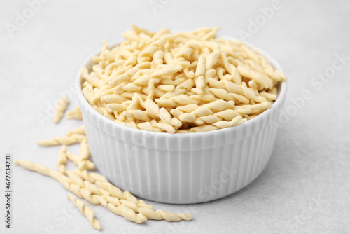 Bowl with uncooked trofie pasta on light grey table, closeup photo