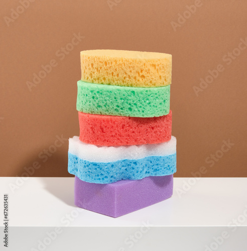 Five colorful shower and bath sponges of different shapes and sizes on a white table.