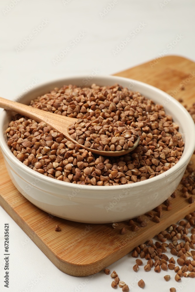 Bowl and spoon with dry buckwheat on white table, closeup Bowl and spoon with dry buckwheat on white table, closeup