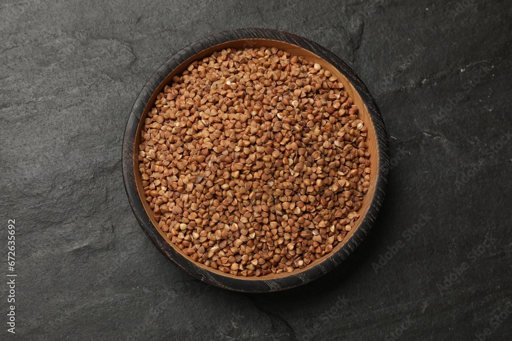 Bowl with dry buckwheat on black table, top view Bowl with dry buckwheat on black table, top view