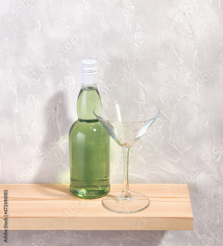 An interestingly shaped glass bottle with a white cap and a green alcohol drink. Empty alcohol glass on the table. Party and holiday composition. photo
