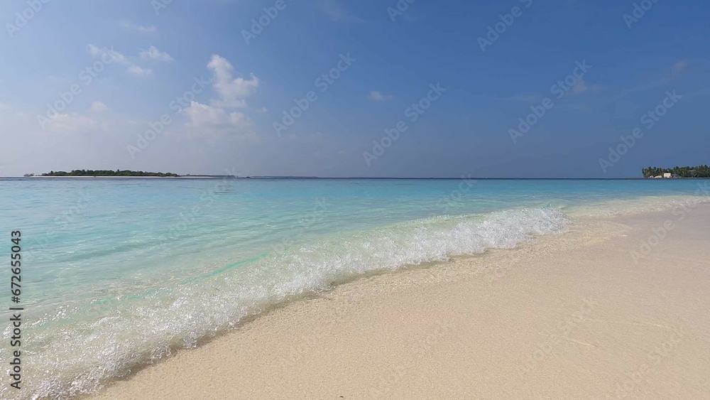 Maldives beach, waves wash the shore with white sand, clear azure water, and blue sky. Beauty, paradise, Indian ocean view