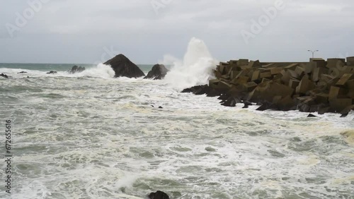 Static shot of rough and dangerous sea in slow motionwith large waves breaking against the harbor and rocks due to a storm and strong winds. 