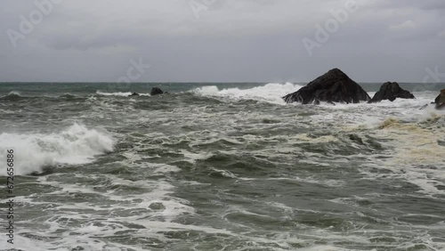 static shot of rough and dangerous sea with large waves breaking against the harbor and rocks due to a storm and strong winds. 