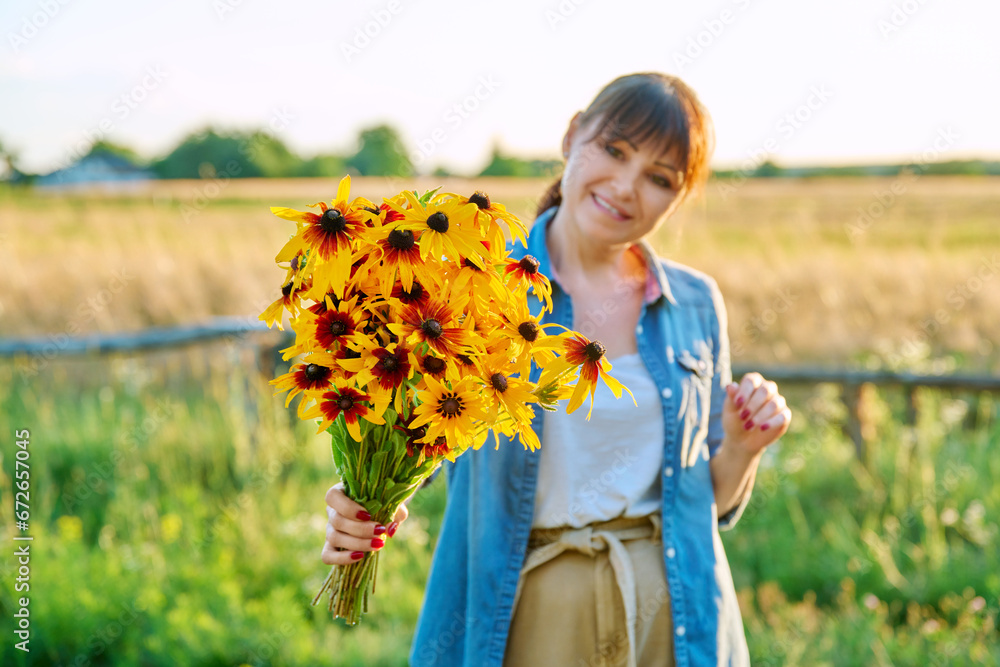 Bouquet of yellow flowers in hands of woman, rural landscape in summer sunset light Bouquet of yellow flowers in hands of woman, rural landscape in summer sunset light