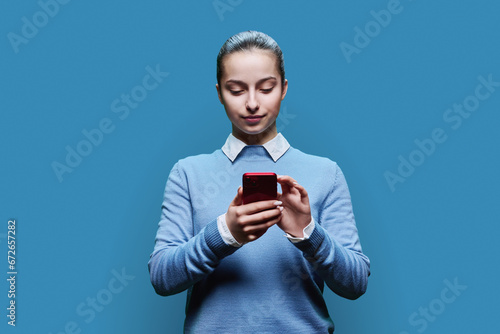 Teenage student girl using smartphone on blue studio background © Valerii Honcharuk