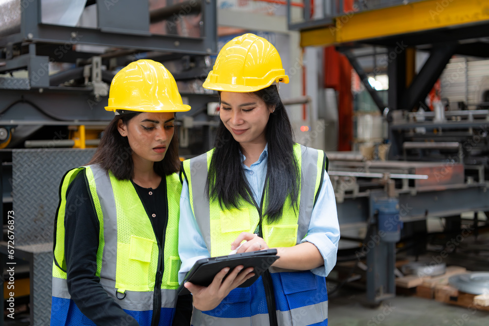 Two female engineers working together in metal sheet factory. This is a freight transportation and distribution warehouse. Industrial and industrial workers concept Two female engineers working together in metal sheet factory. This is a freight transportation and distribution warehouse. Industrial and industrial workers concept