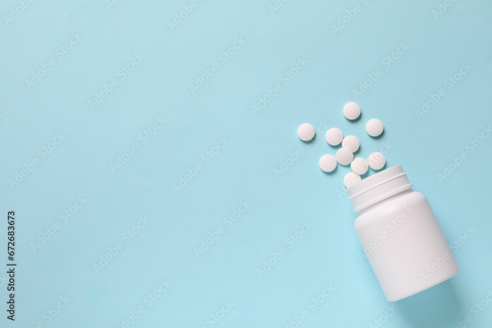 Plastic bottle with many white pills on light blue background, flat lay. Space for text