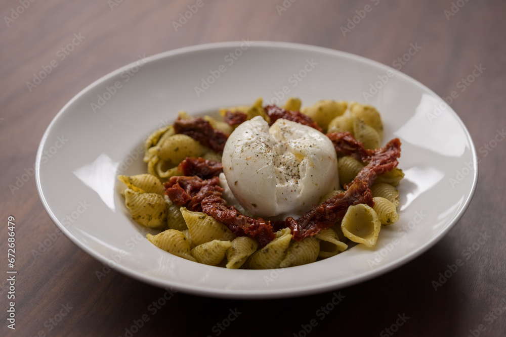 Pesto conchiglie with sundried tomatoes and burrata cheese served in white plate