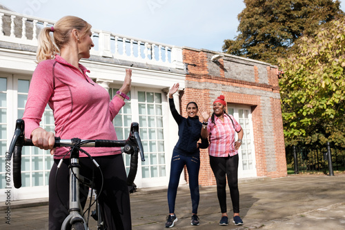 Woman on a bike waving her fitness mature friends after exercise.