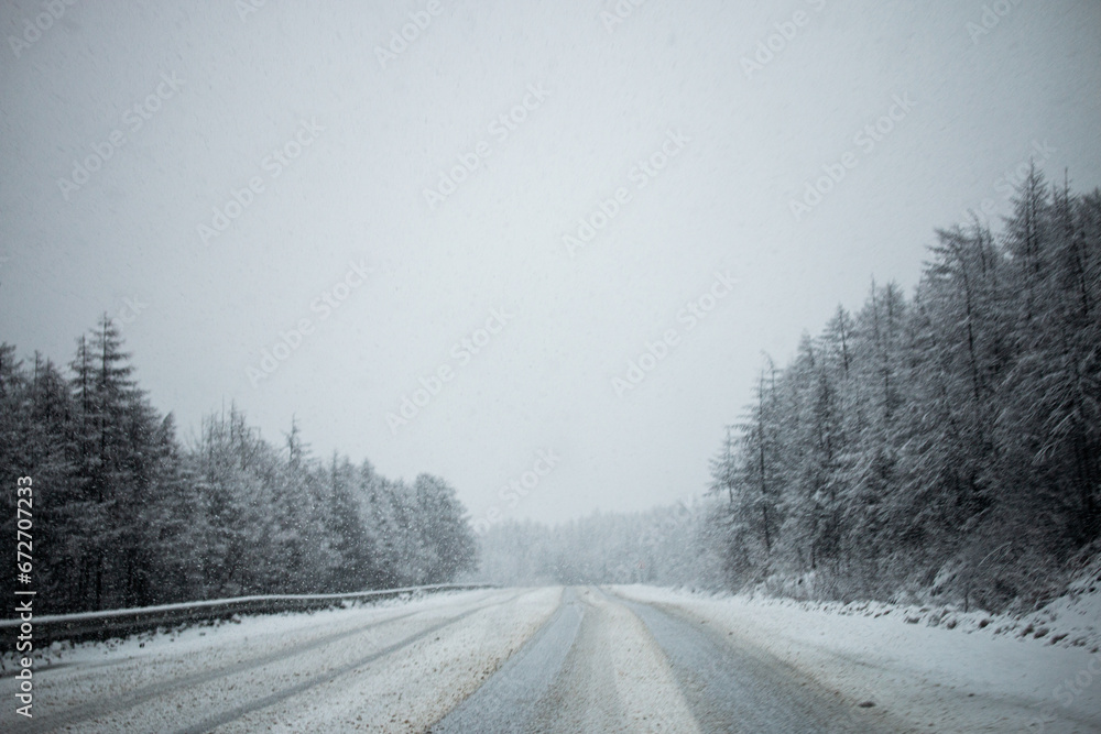 Photo of the winter road during the snowfall in Magadan, Russia. Snow showers on the trees and hills. Slush on the way. Fog and haze, low visibility due to snowstorm. Extreme weather conditions