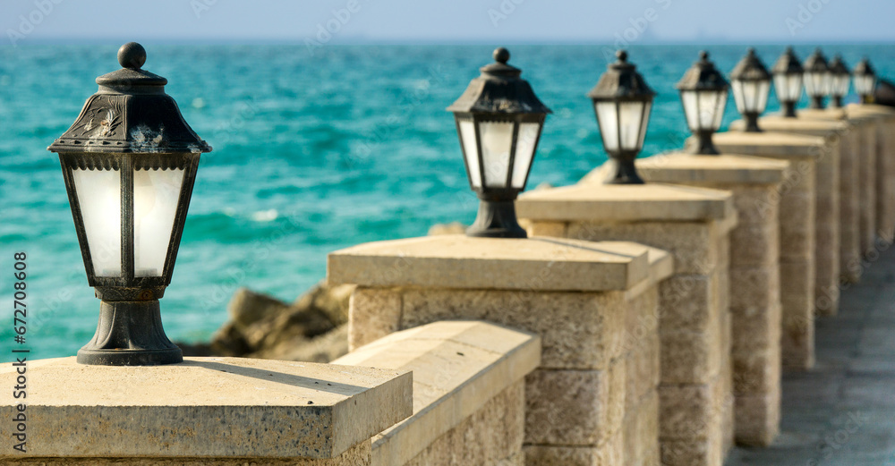 Embankment and white vintage lanterns, on a stone wall, against the backdrop of the turquoise sea