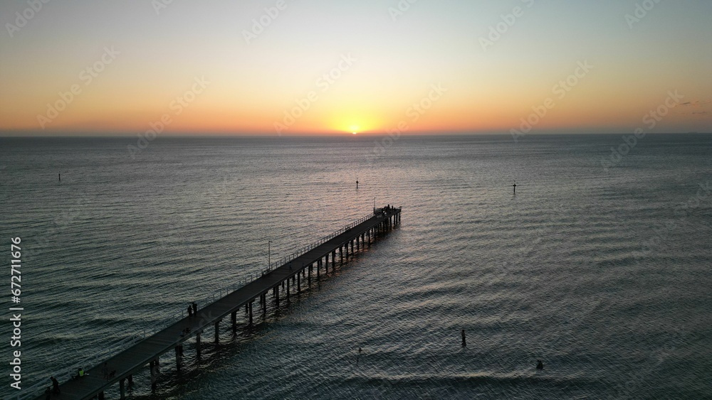 Aerial view of the pier and tranquil sea with a stunning sunset in the background.