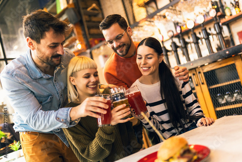 Smiling young friends drinking craft beer in pub