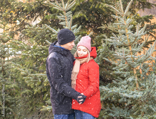 Happy woman and man hugging at Christmas Market in front of Christmas tree at a snowing day.