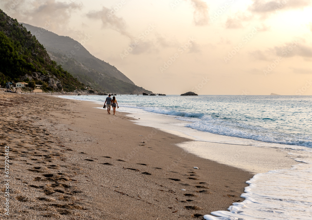 A couple on holiday walking on a beautiful long sandy beach.