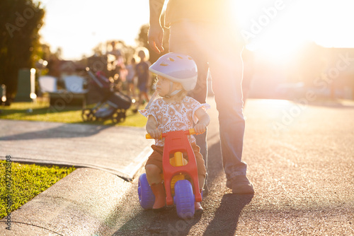 Young Aussie kid playing on trike on street at sunset with parent watching photo
