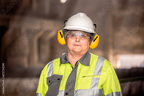 A worker in a helmet and equipment stands against the backdrop of a cement plant workshop. Work technology, cement production. People working in heavy industry.