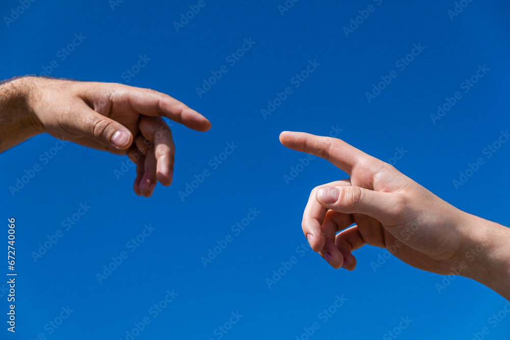 index fingers stretching to each other against the background of the sky