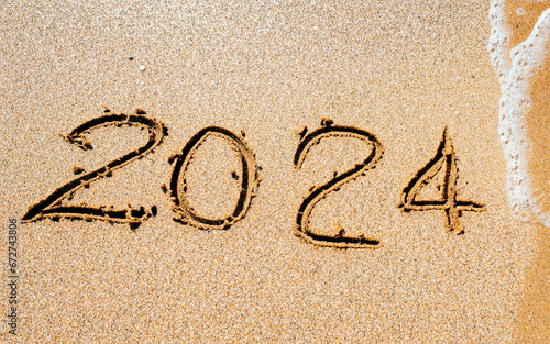Símbolo do novo ano de 2024. Novo ano de 2024 desenhado na areia da praia. A onda lavará a inscrição 2024 photo