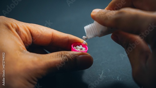 Young adult person placing colorful pills onto his fingers while seated at a table photo