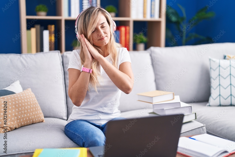Young blonde woman studying using computer laptop at home sleeping tired dreaming and posing with hands together while smiling with closed eyes. Young blonde woman studying using computer laptop at home sleeping tired dreaming and posing with hands together while smiling with closed eyes.